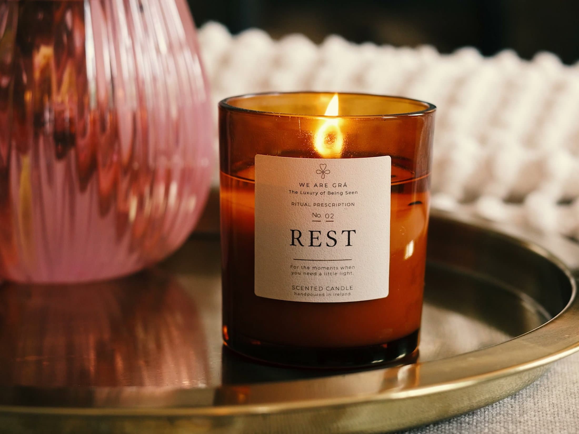 Lit Rest candle from We Are Grá beside a blush glass vase.